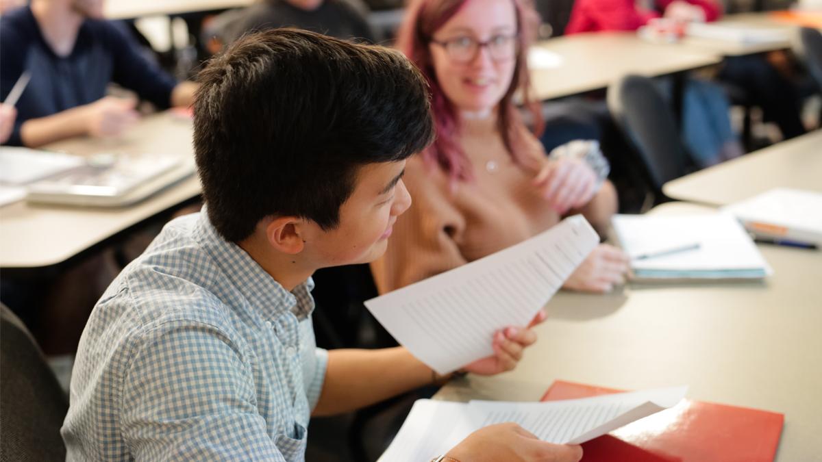 Male student holds a piece of paper in a classroom setting.